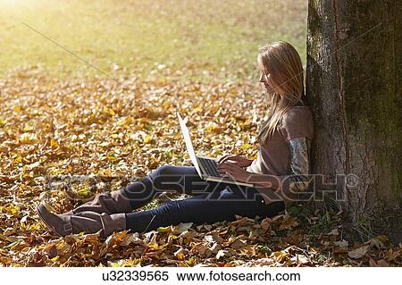 Stock Photography - Woman using laptop in autumn leaves. Fotosearch