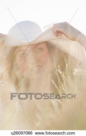 Stock Photograph - Woman wearing sun hat in tall grass. Fotosearch