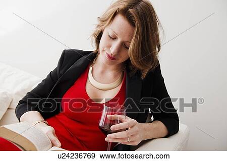 Stock Photo - Woman with wine reading book on sofa. Fotosearch