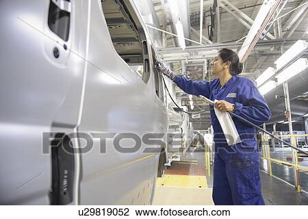Stock Image - Worker applying sealant in car factory. Fotosearch