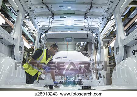 Stock Image - Worker fitting parts in car factory. Fotosearch