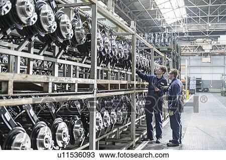 Stock Image - Workers inspecting axles in car factory. Fotosearch