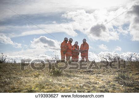 Stock Photo - Workers reading blueprints in field. Fotosearch