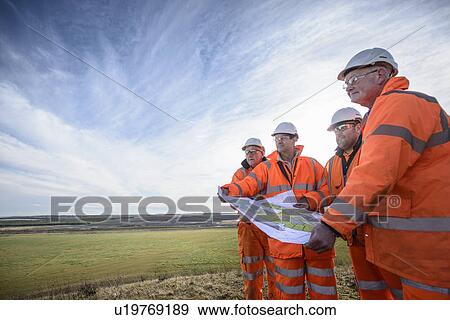 Stock Photo - Workers reading blueprints in field. Fotosearch