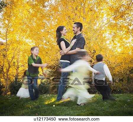 Stock Image - Bountiful, Family with children (2-3, 4-5, 6-7, 8-9) dancing in garden at autumn. Fotosearch