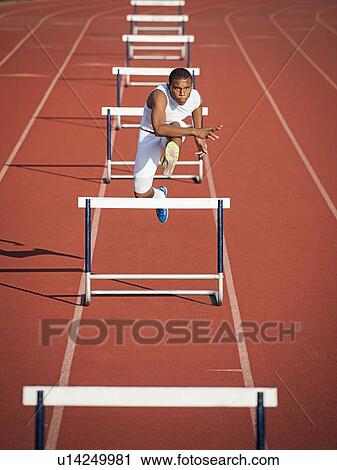 Stock Image - Boy (12-13) hurdling on running track. Fotosearch