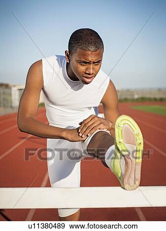 Boy (12-13) stretching on hurdle on running track View Large Photo Image Stock Photo - Boy (12-13) stretching on hurdle on running track. Fotosearch