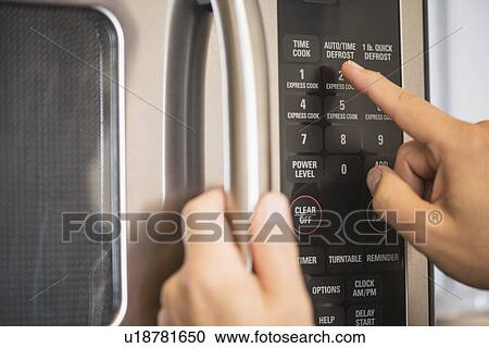 Stock Image - Close-up of hand using microwave oven. Fotosearch