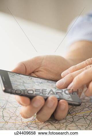 Stock Photo - Close-up of hand using smartphone over map. Fotosearch