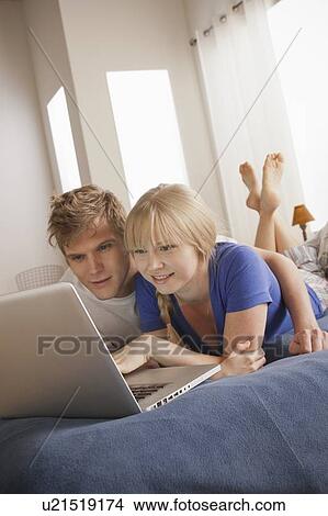 Picture - Couple lying on bed using laptop. Fotosearch