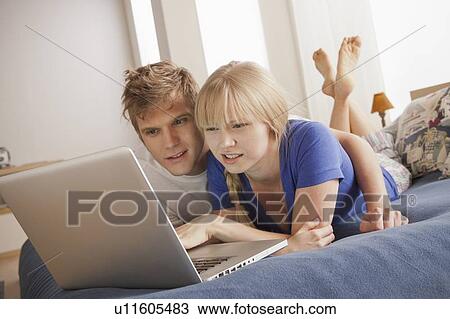 Stock Image - Couple lying on bed using laptop. Fotosearch