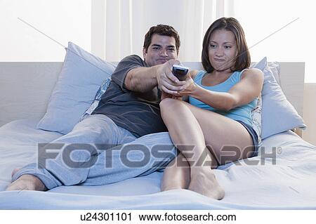 Stock Image - Couple sitting on bed and watching tv. Fotosearch