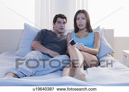 Couple sitting on bed and watching tv View Large Photo Image Stock Photo - Couple sitting on bed and watching tv. Fotosearch