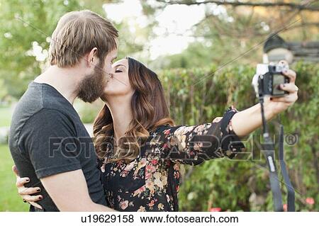 Stock Photo - Couple taking picture while kissing. Fotosearch