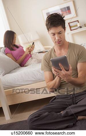 Stock Image - Couple using mobile phone and digital tablet. Fotosearch