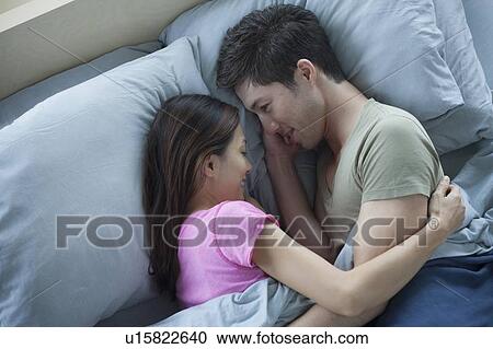 Stock Image - Elevated view of man and woman embracing in bed. Fotosearch