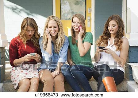 Stock Image - Four friends sitting on porch with their mobile phones. Fotosearch