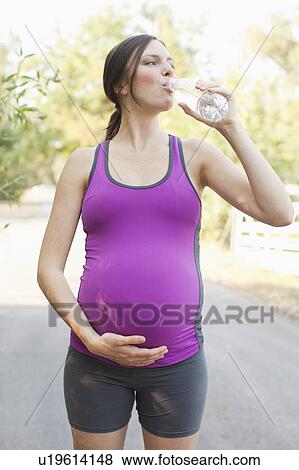 Front view of pregnant mid adult woman in sport clothing drinking water View Large Photo Image Stock Photo - Front view of pregnant mid adult woman in sport clothing drinking water. Fotosearch