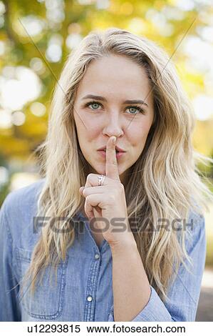 Stock Photography - Front view portrait of young woman with finger on lips. Fotosearch