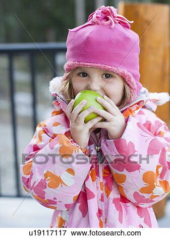 Stock Photo - Girl (4-5) wearing warm clothing eating outdoors. Fotosearch