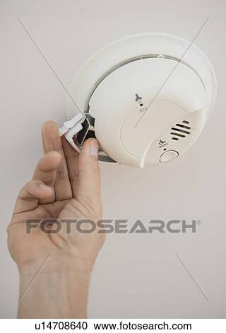 Stock Image - Hand changing battery in smoke alarm. Fotosearch