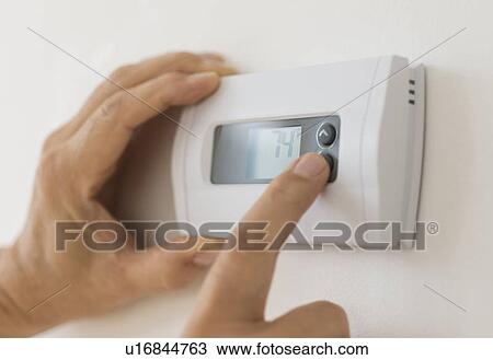 Stock Image - Hand changing settings on air conditioning thermostat. Fotosearch