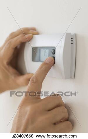 Stock Photo - Hand changing settings on air conditioning thermostat. Fotosearch
