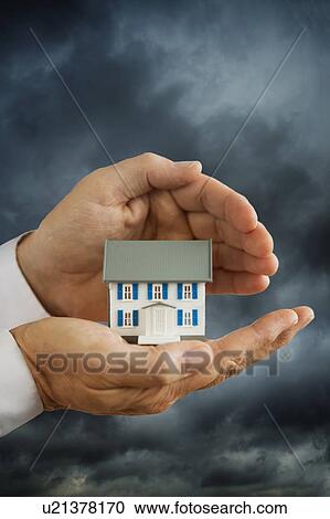 Stock Image - Hands holding model house in front of stormy sky. Fotosearch
