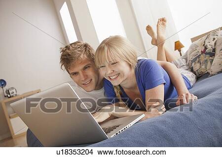Happy couple lying on bed using laptop View Large Photo Image Picture - Happy couple lying on bed using laptop. Fotosearch