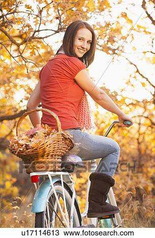Stock Image - Happy young woman with bicycle in autumn in forest. Fotosearch