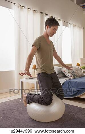 Stock Photograph - Man kneeling on top of fitness ball. Fotosearch