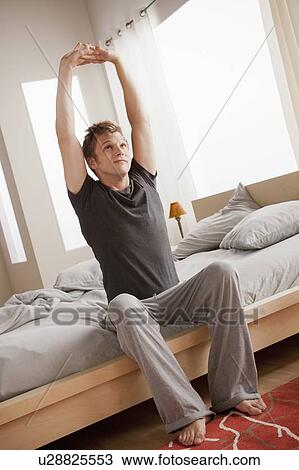 Stock Image - Man sitting on bed and stretching. Fotosearch