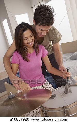 Stock Image - Man teaching woman how to play drums. Fotosearch