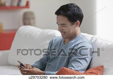 Stock Image - Man texting in living room. Fotosearch