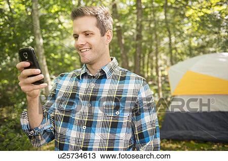 Stock Image - Man using cell phone in forest. Fotosearch