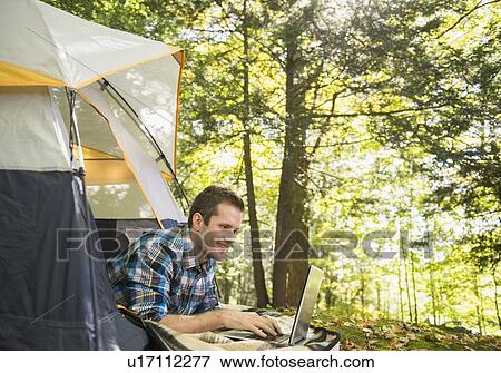 Stock Photo - Man using laptop outside tent. Fotosearch