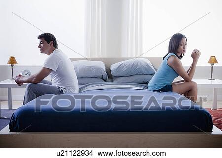 Picture - Mid adult couple after quarrel sitting on bed. Fotosearch