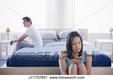 Stock Image - Mid adult couple after quarrel sitting in bedroom. Fotosearch