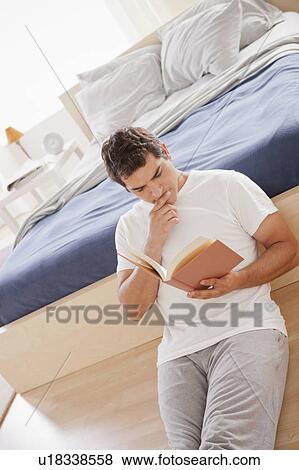 Mid adult man reading book sitting on bedroom floor View Large Photo Image Stock Photo - Mid adult man reading book sitting on bedroom floor. Fotosearch