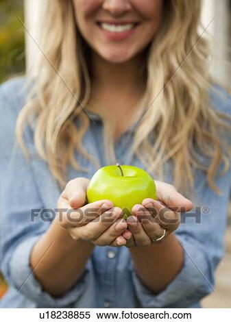 Stock Photography - Mid-section of young woman holding green apple. Fotosearch