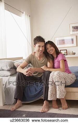 Stock Photograph - Portrait of couple sitting on bed. Fotosearch