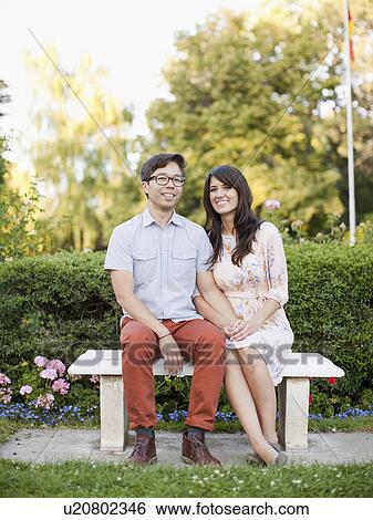 Stock Photograph - Portrait of couple sitting on bench in park. Fotosearch