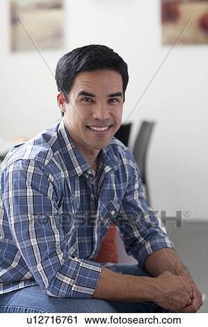 Stock Image - Portrait of man sitting in living room. Fotosearch
