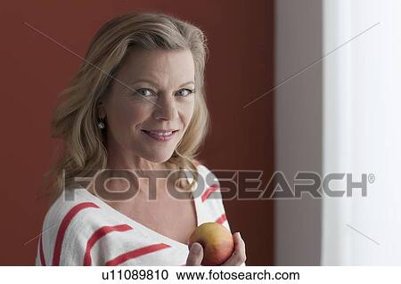 Stock Image - Portrait of mature woman eating apple. Fotosearch