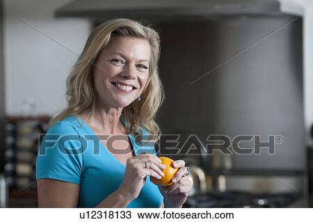 Stock Image - Portrait of mature woman eating orange. Fotosearch