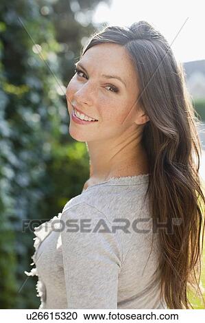 Stock Image - Portrait of mid adult woman looking over shoulder. Fotosearch