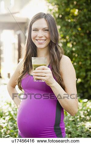 Stock Photograph - Portrait of pregnant mid adult woman in sport clothing holding glass with green juice. Fotosearch