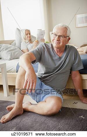 Stock Image - Portrait of senior man, woman sitting on bed in background. Fotosearch