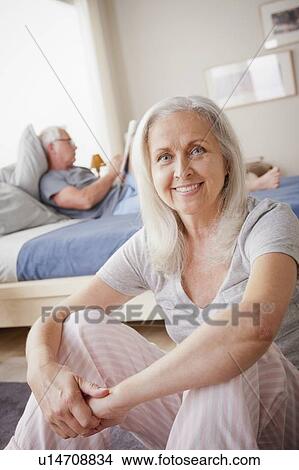 Picture - Portrait of senior woman, man sitting on bed in background. Fotosearch