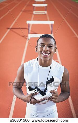 Stock Image - Portrait of smiling boy (12-13) leaning on hurdle on running track. Fotosearch
